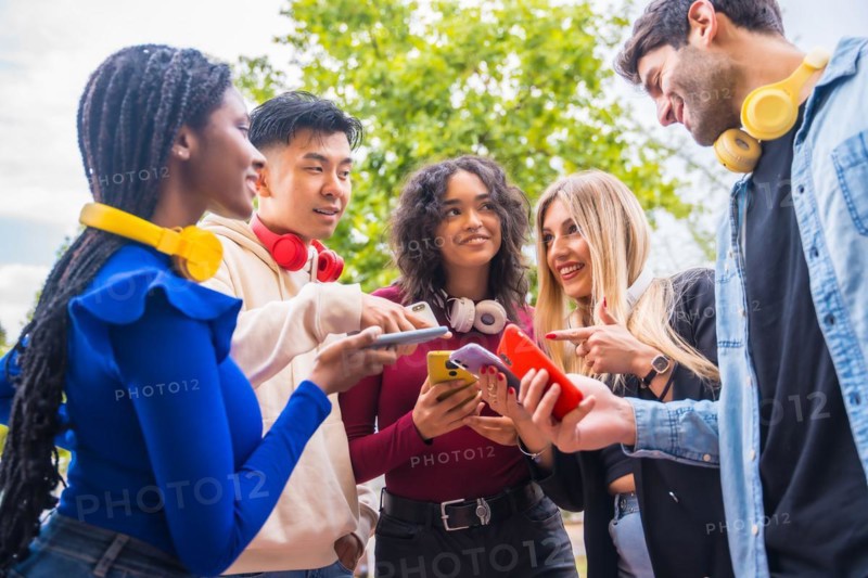 Group of young smiling teenage multiethnic friends using cell phones on campus in the city