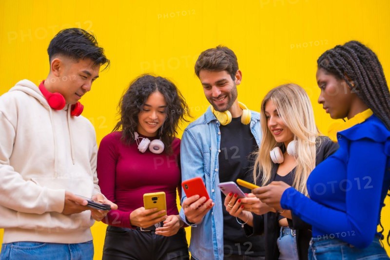 Low angle view of a group of young multi-ethnic teenage friends using cell phones on a yellow background