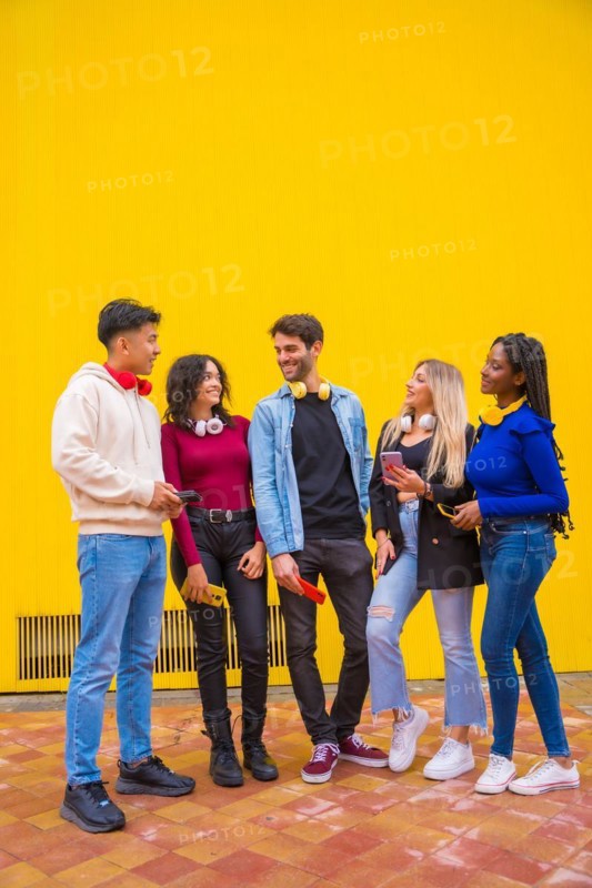Portrait of a group of smiling young multi-ethnic teenage friends using cell phones on a yellow background