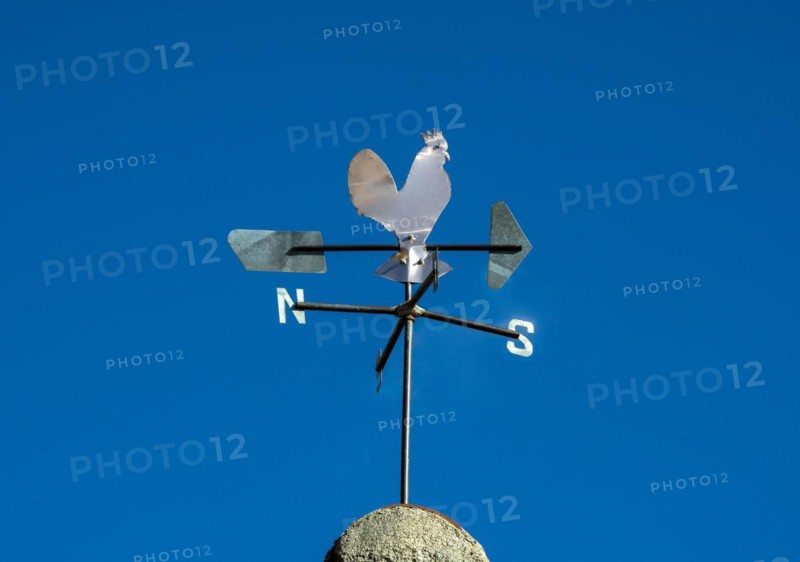 Weathercock in the shape of a rooster on a blue sky