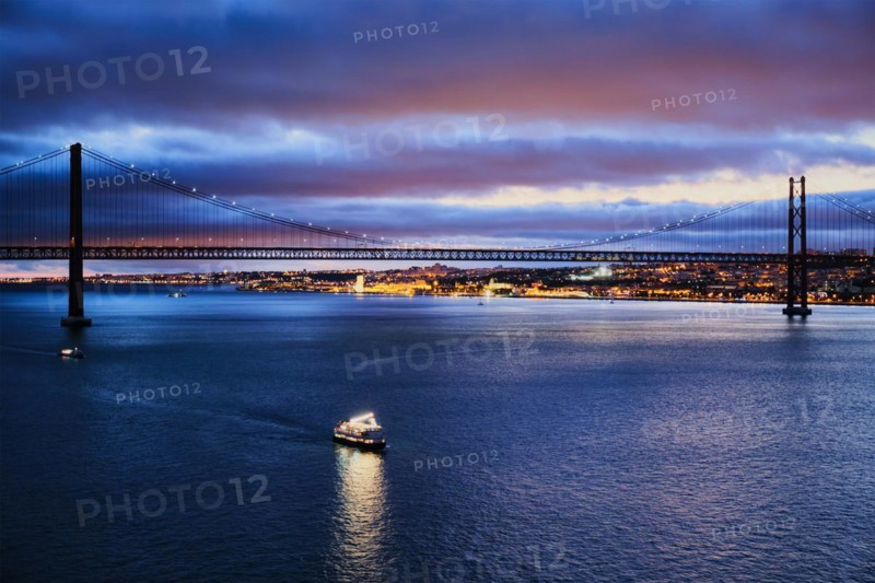 View of 25 de Abril Bridge famous tourist landmark of Lisbon connecting Lisboa and Almada on Setubal Peninsula over Tagus river in the evening twilight with tourist boats