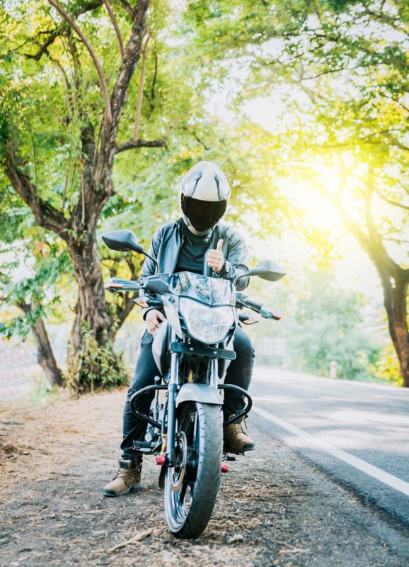 Motorcyclist in safety helmet with thumb up on the road