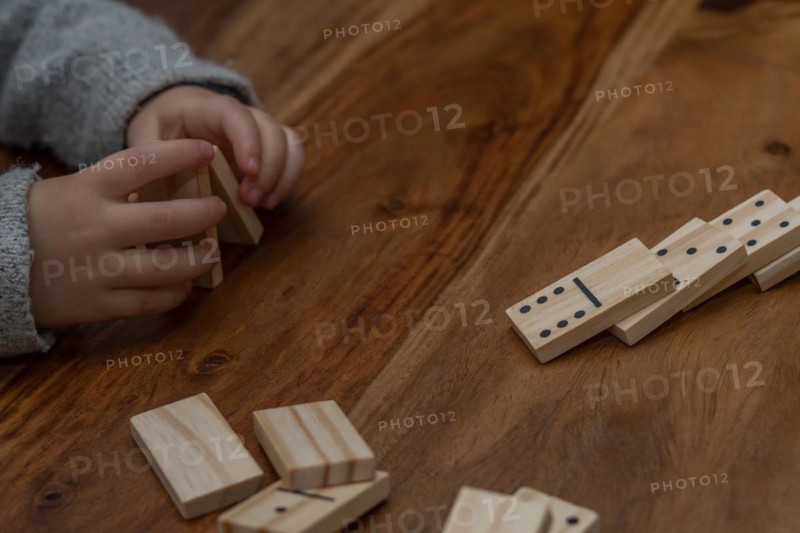 Child's hands in gray sweater playing dominoes with blurred focus