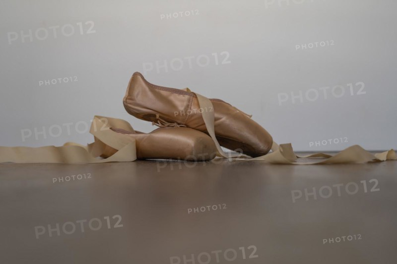 Ballet slippers with orange ribbon on a wooden floor and white background