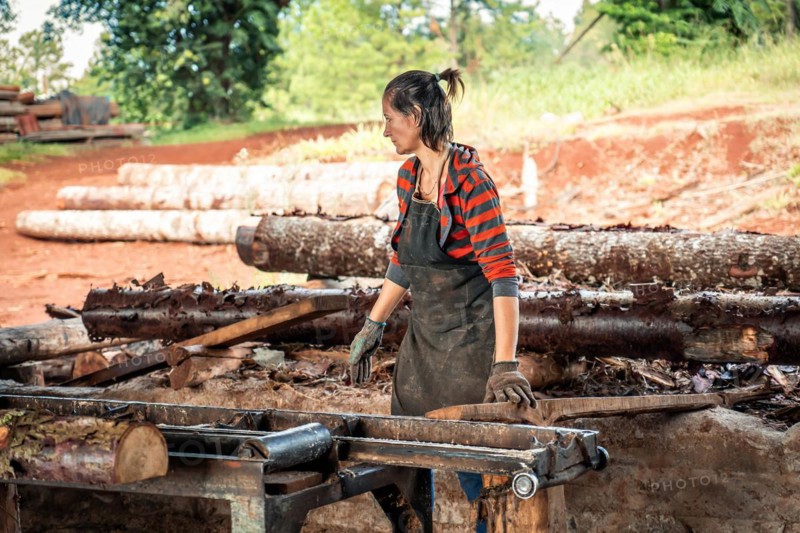 Woman in work clothes carrying a large log in a sawmill