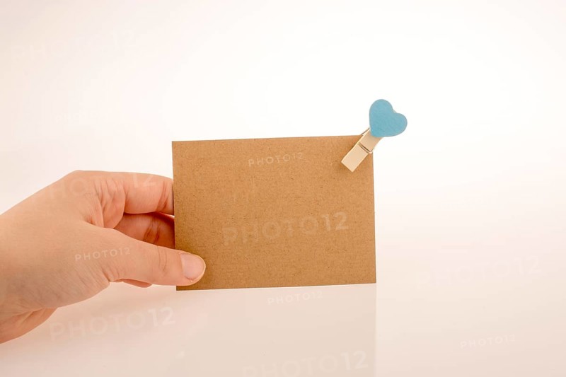 Hand holding a paper placed in a clothespin withe heart on a white background