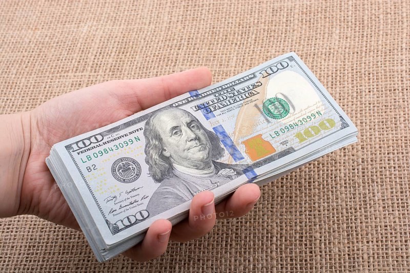 Hand holding banknote bundle of US dollar on a linen canvas background