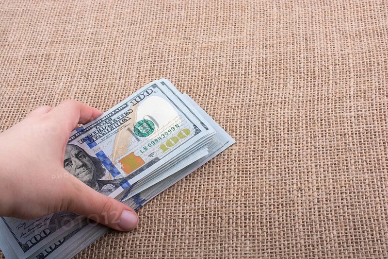 Hand holding banknote bundle of US dollar on a linen canvas background