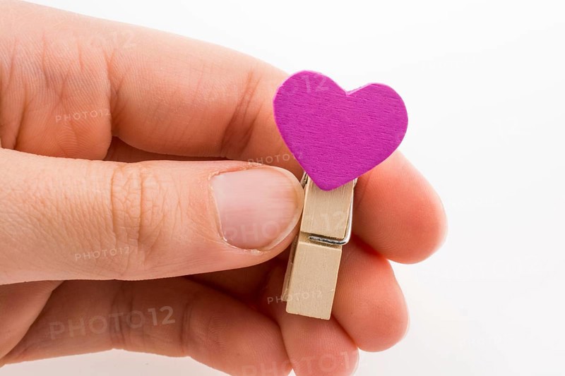 Hand holding a red clothespin with a heartshape on a white background