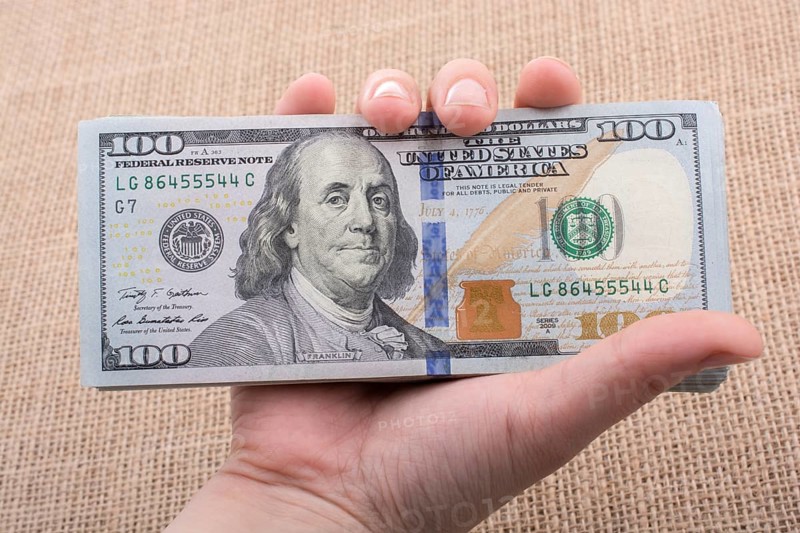Hand holding banknote bundle of US dollar on a linen canvas background