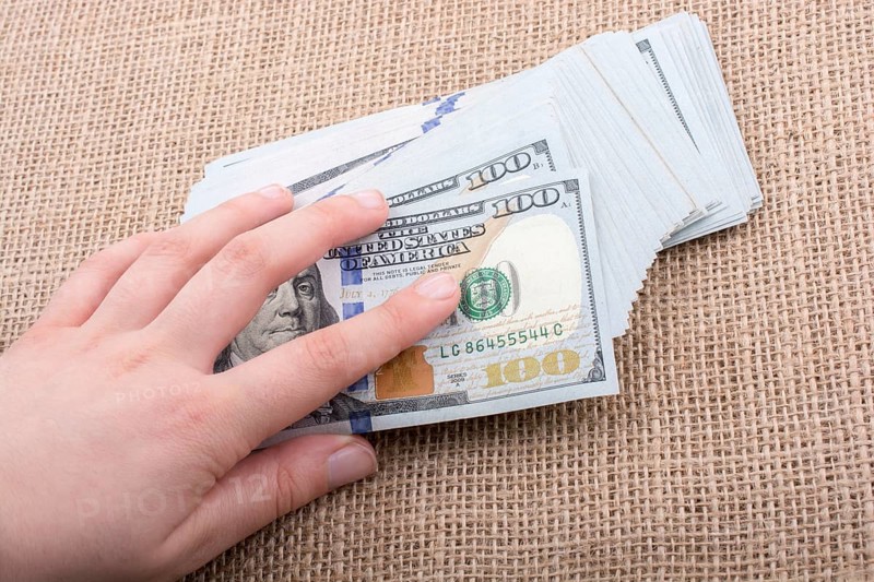 Hand holding banknote bundle of US dollar on a linen canvas background