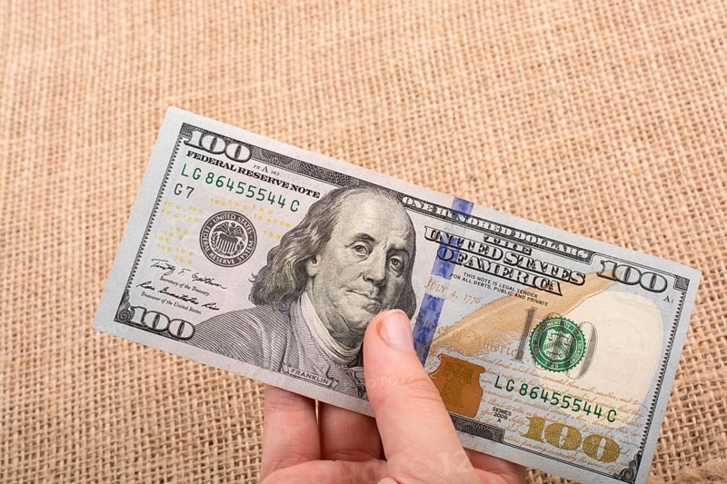 Hand holding banknote bundle of US dollar on a linen canvas background