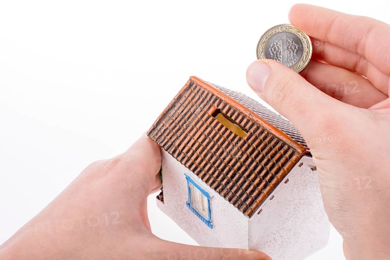 Hand dropping coin into the moneybox in the shape of a model house