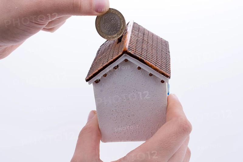 Hand dropping coin into the moneybox in the shape of a model house
