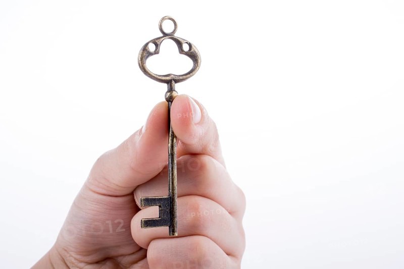 Hand holding a retro styled metal key on a white background