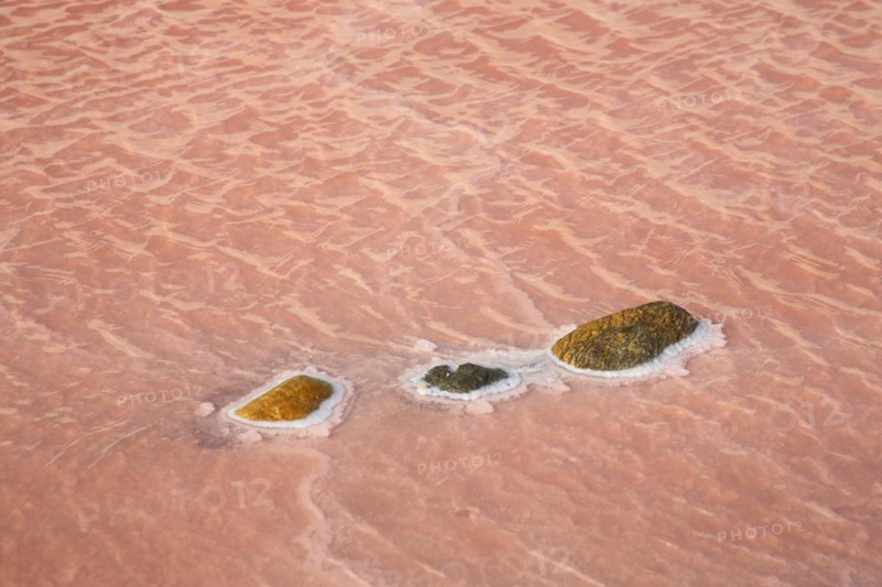 Red salt water with three stones with salt deposit at saline