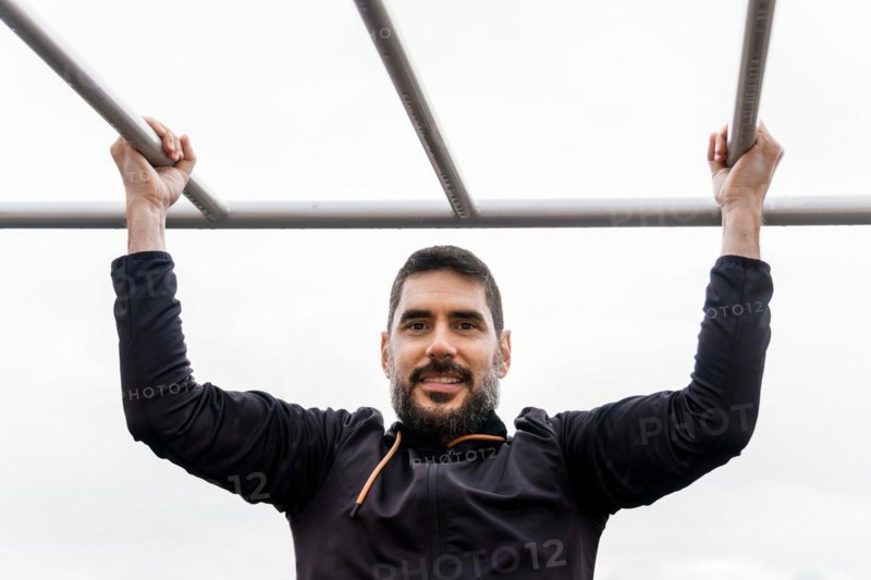 Young man dressed in black training on a pull-up bar in an outdoor gym