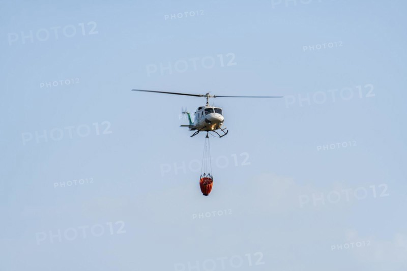 Firefighting helicopter in mid-flight dropping water bag on flames