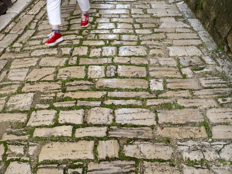 A woman with red shoes walks on a cobblestone street
