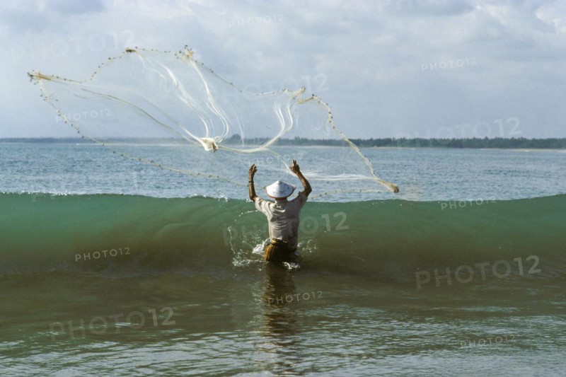 Fisherman with cast net in front of wave