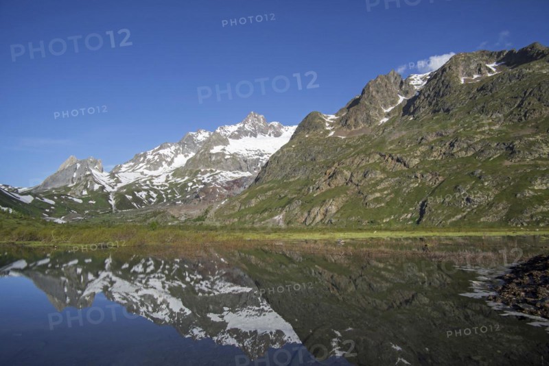 Reflection of mountains of the Mont Blanc massif and the Limestone Pyramids in water of Lago Combal lake in Val Veny in the Italian Alps
