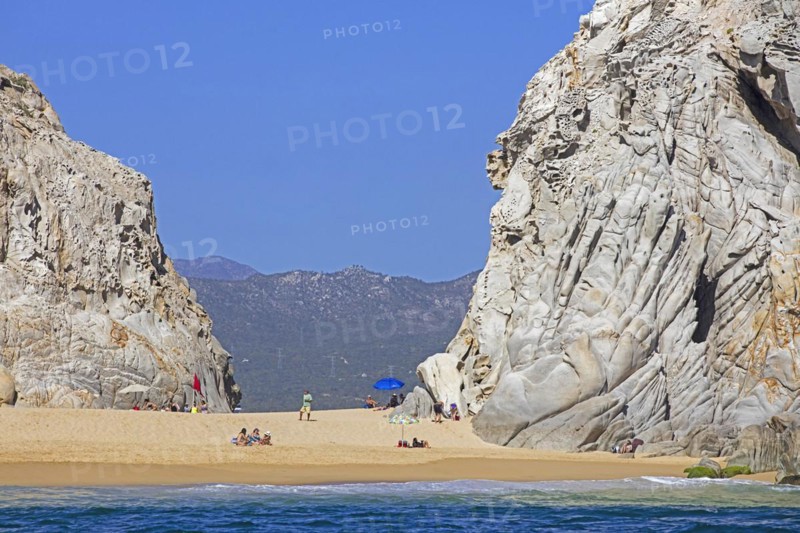 Limestone sea cliffs and tourists sunbathing on secluded beach near the seaside resort Cabo San Lucas on the peninsula of Baja California Sur