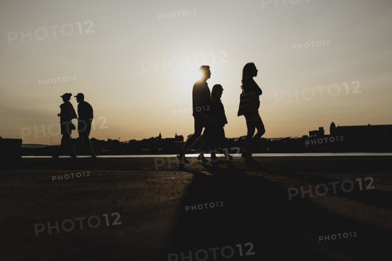 Silhouettes of walkers stand out against the setting sun on the harbour promenade in Oslo