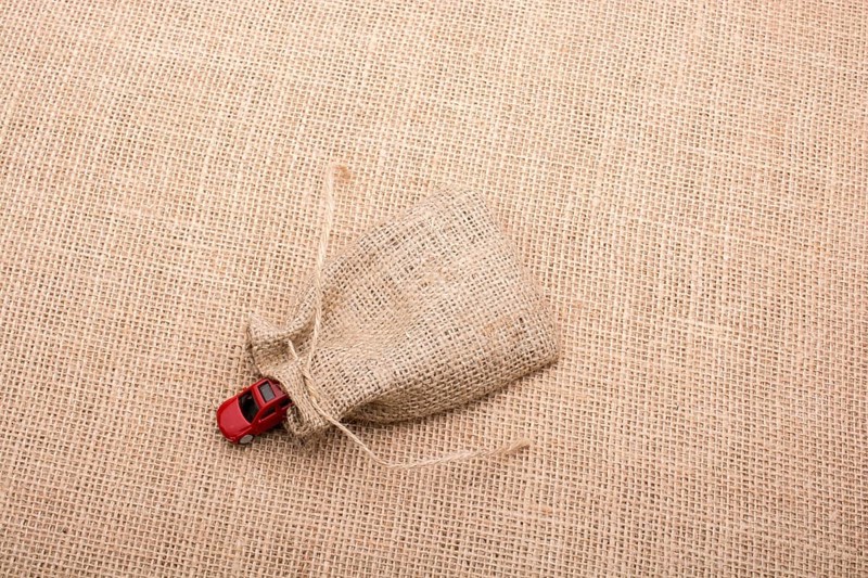 Red toy car coming out of a linen sack on a linen canvas