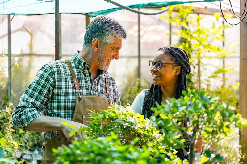 Master gardener teaching schoolgirl flower nursery in greenhouse smiling