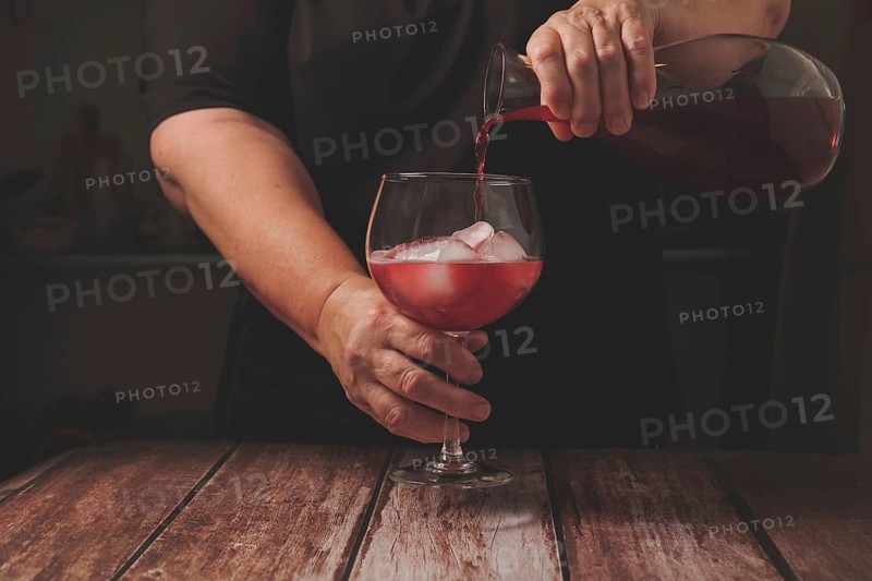 Waitress dressed in black serving a glass of sparkling red summer wine on the rocks from a glass decanter