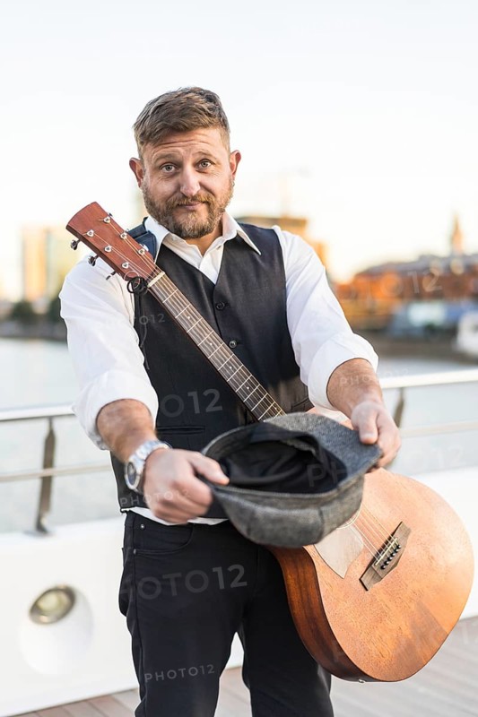 A street musician looking at camera and carrying his guitar while asking for tips