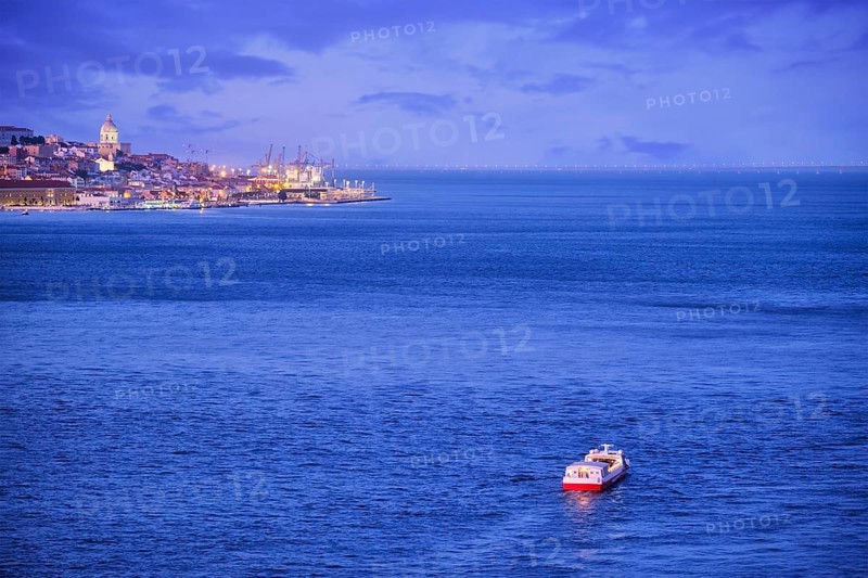 Night view of Lisbon over Tagus river from Almada with ferry and tourist boat in evening twilight. Lisbon