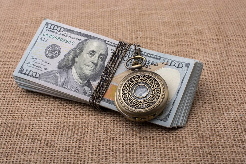 Pocket watch wrapped around banknote bundle of US dollar