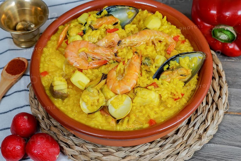 Appetizing typical spanish seafood paella in an earthenware casserole surrounded by some of its ingredients