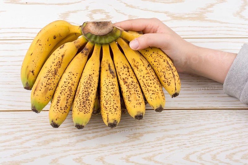 Hand holding bunch of freckled bananas on a wooden texture