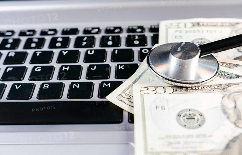 Stethoscope on dollar bills on top of laptop keyboard. Stethoscope on top of money on laptop keyboard