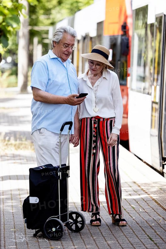 Elderly couple waiting for the tram at a stop with a smartphone in hand