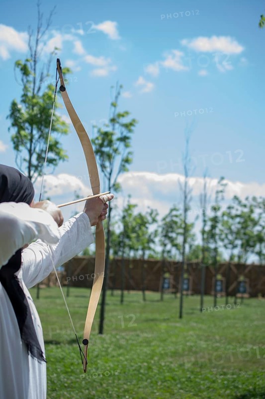 Archer with bow in traditional clothes shooting an arrow