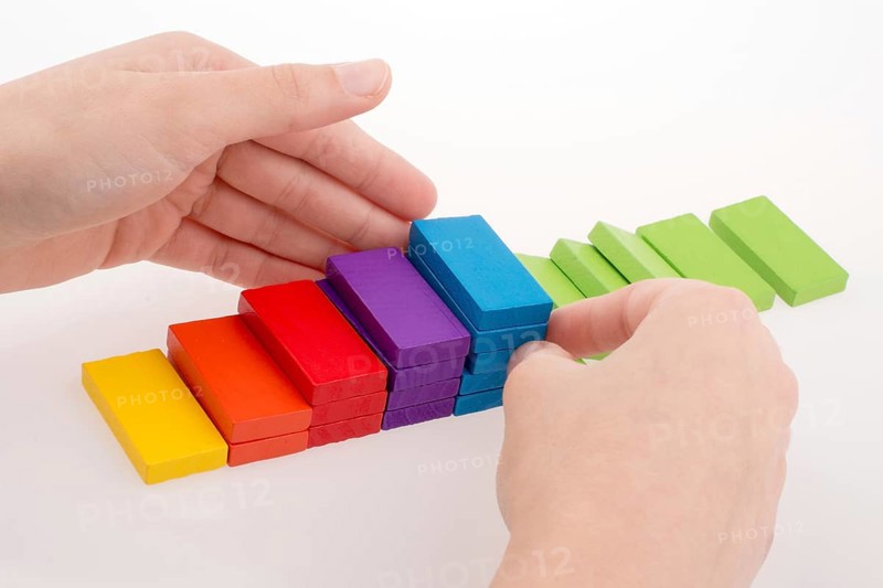 Hand playing with colored domino on white background