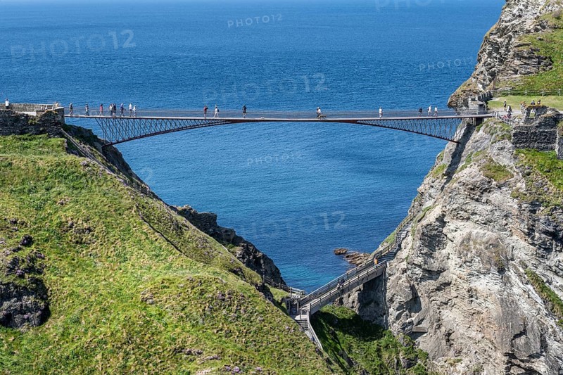 Tourists walk across the new footbridge to the peninsula with the castle ruins of Tintagel Castle