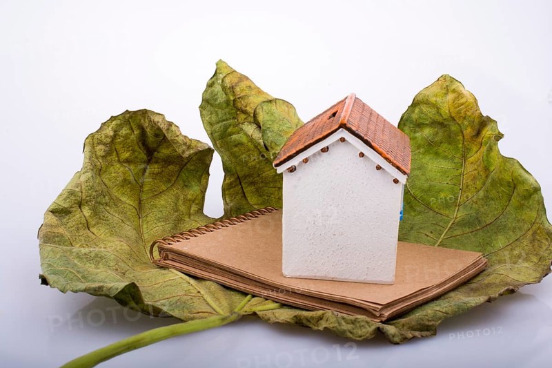 Little model house placed on an Autumn leaf and a brown notebook