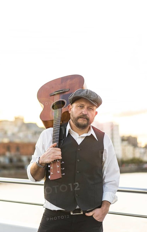 Portrait of a musician looking at camera while holding his guitar on his shoulder