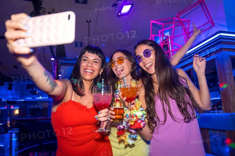 Friends with glasses of alcohol in a nightclub taking a selfie at a night party in a pub