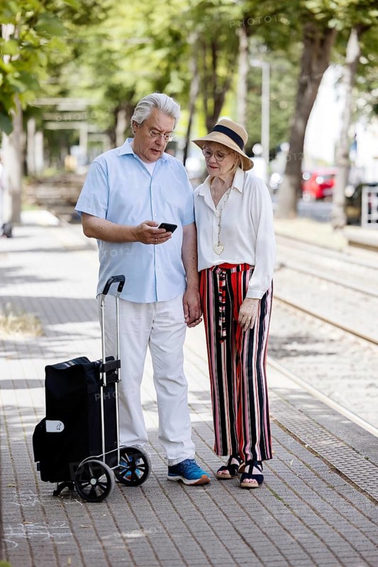 Elderly couple waiting for the tram at a stop with a smartphone in hand