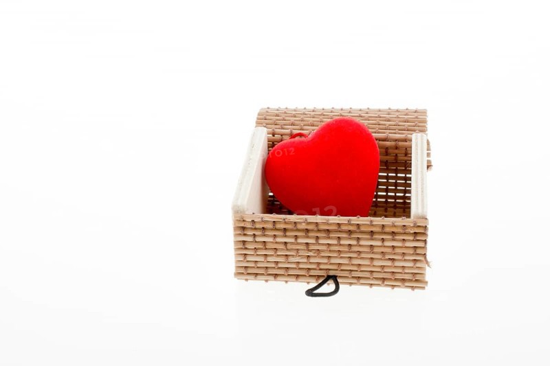 Red heart shaped object placed in a straw box on white background
