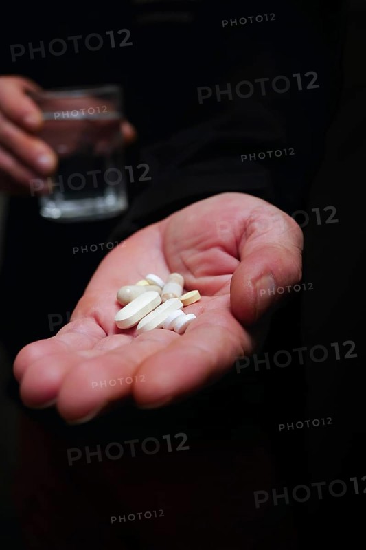 Person in semi-darkness with pills in one hand and a glass of water in the other black background and copy space