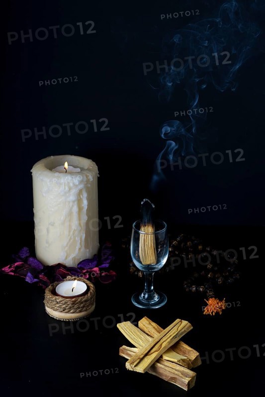 Burning palo santo in a glass cup accompanied by white lighted candles and a Tibetan mala