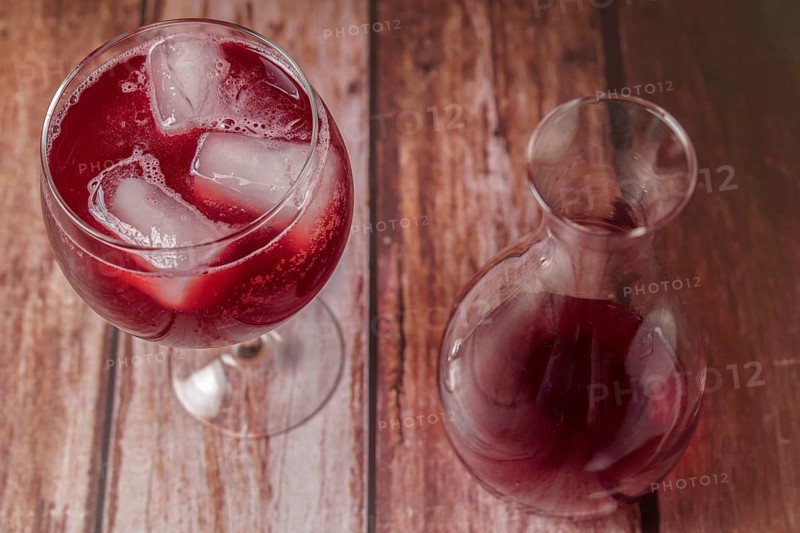 Top view of a sparkling glass of summer red wine on the rocks next to a decanter on a wooden table