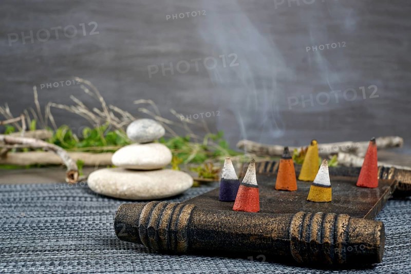 Colorful incense cones burning and smoking on a wooden tray with stacked zen stones