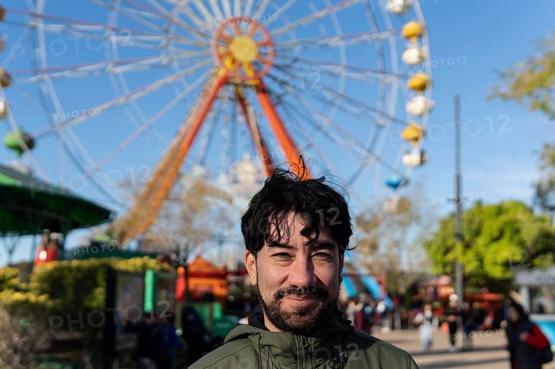 Portrait of latino man in an amusement park posing happy with the ferris wheel in the background